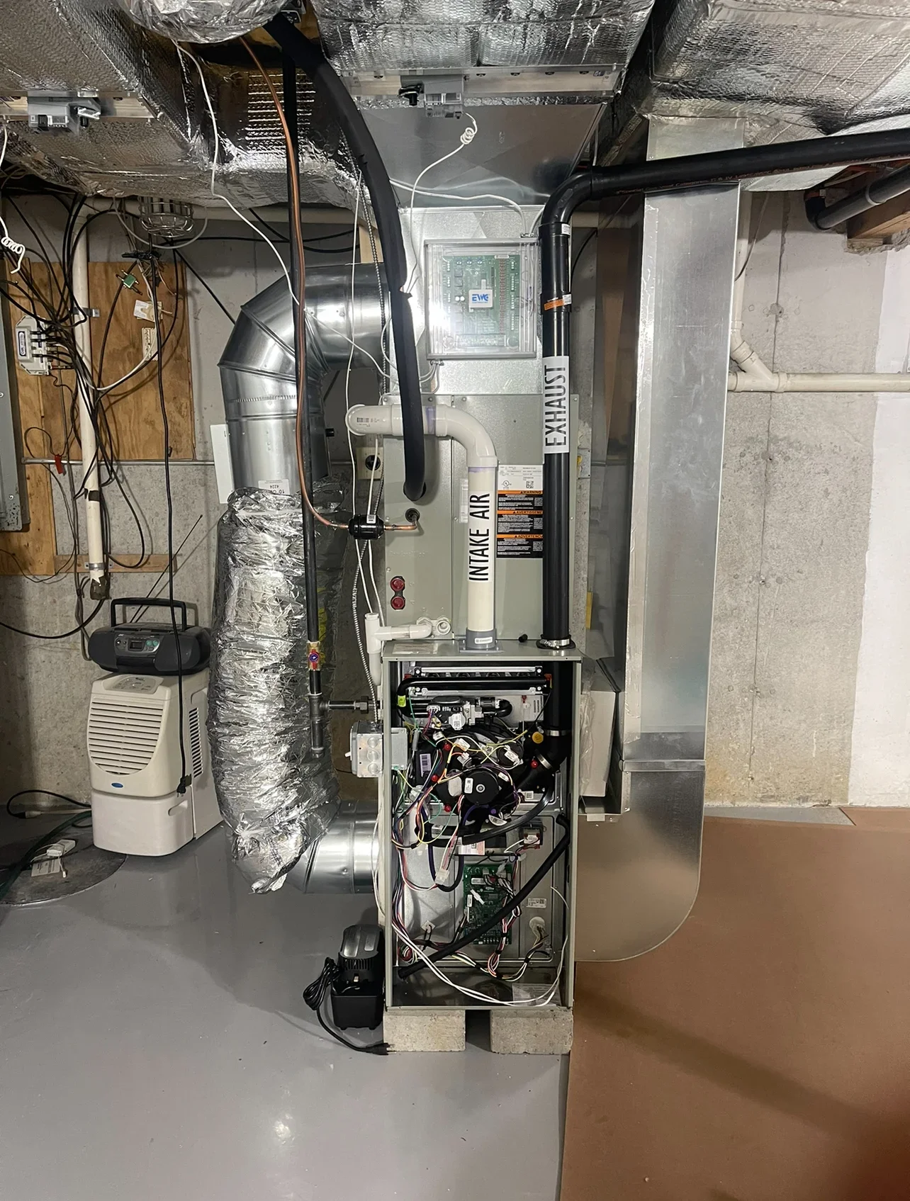 Installed furnace with insulated ductwork, exhaust piping, electrical controls, and dehumidifier in basement