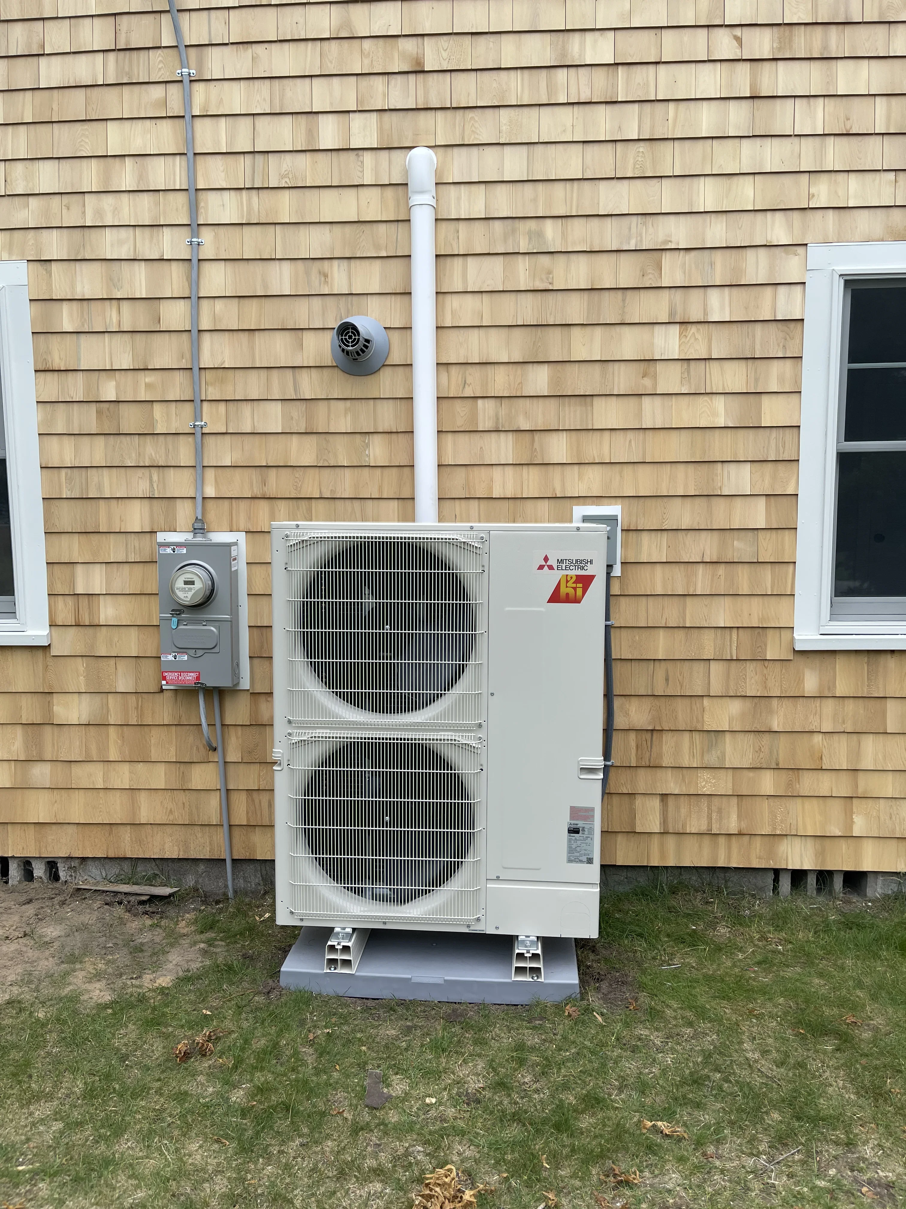 Mitsubishi Electric dual-zone heat pump outdoor unit installed on concrete pad with PVC piping and disconnect switch