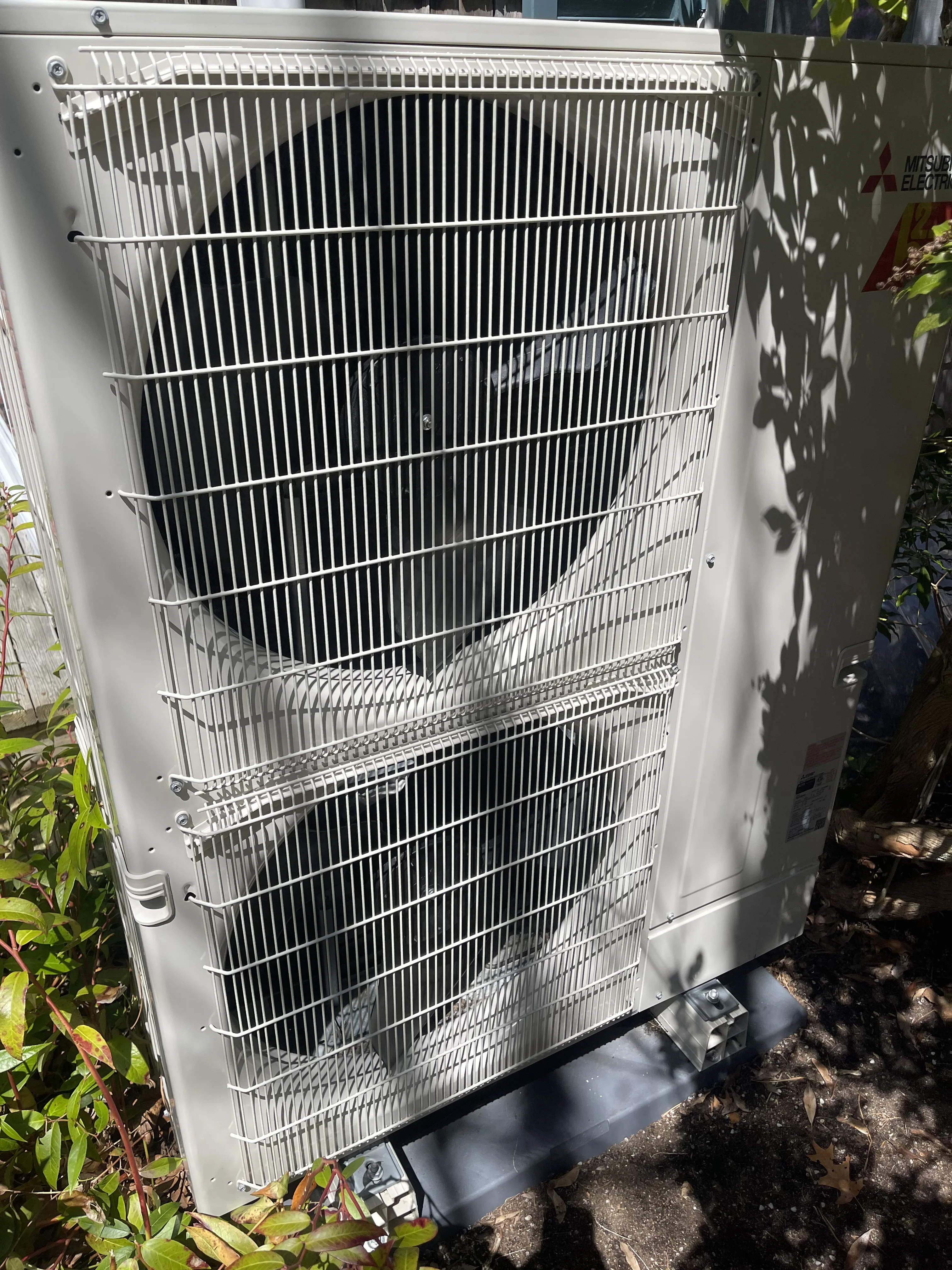 White AC condenser unit with vertical aluminum fins and metal mounting brackets installed outdoors