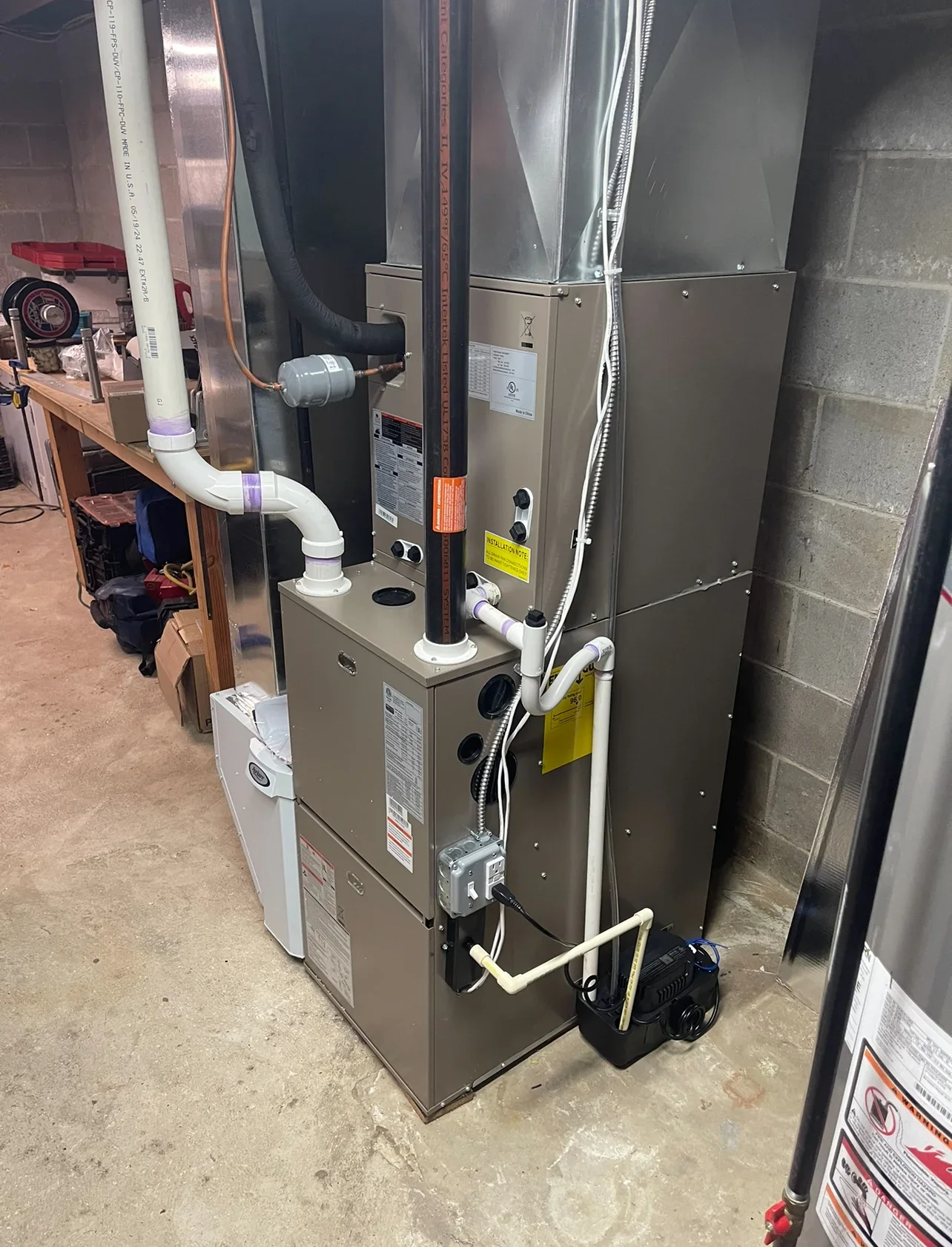 New high-efficiency furnace with white PVC venting, condensate pump, and ductwork connections installed in basement