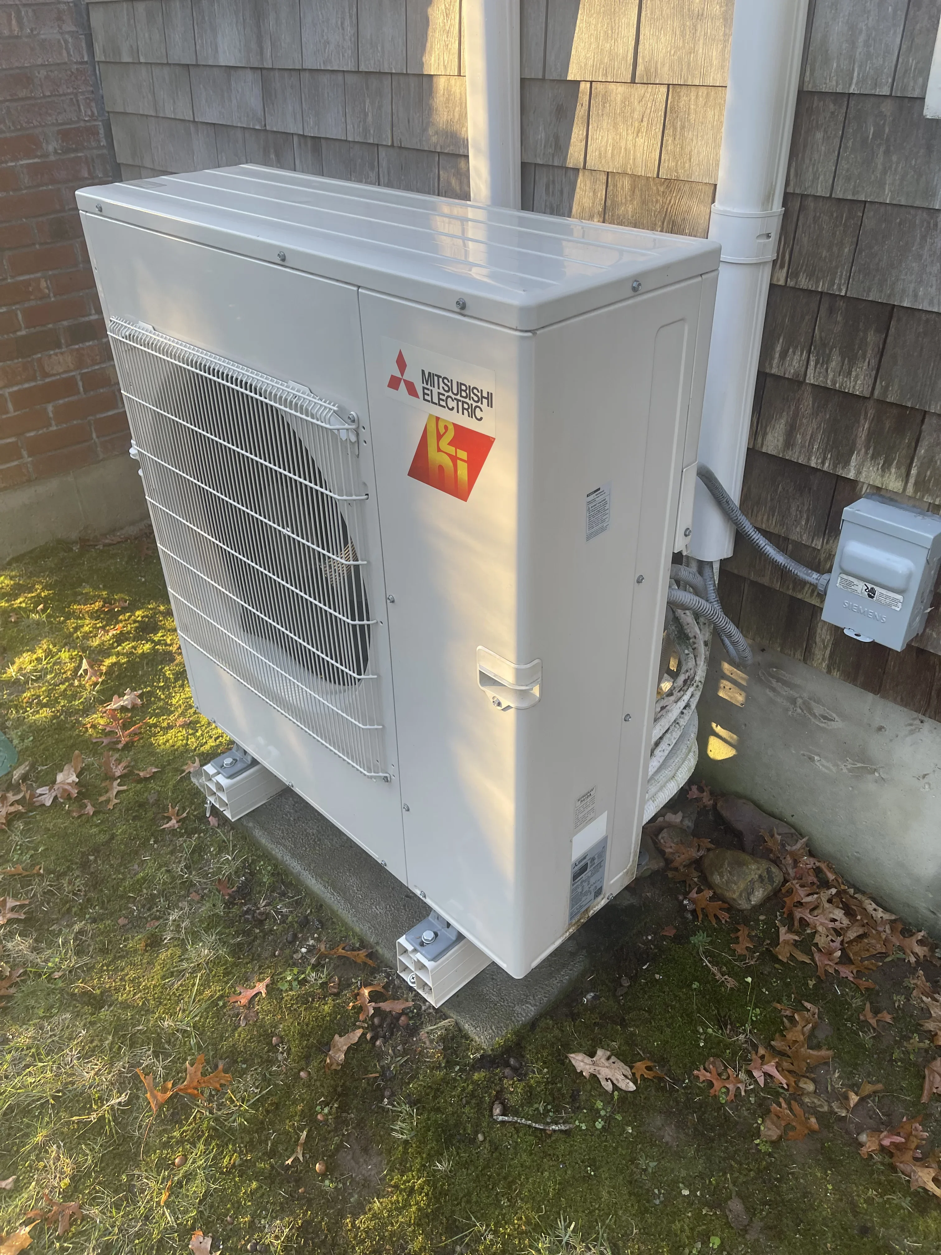 White Mitsubishi Electric heat pump outdoor unit installed on concrete pad with refrigerant lines