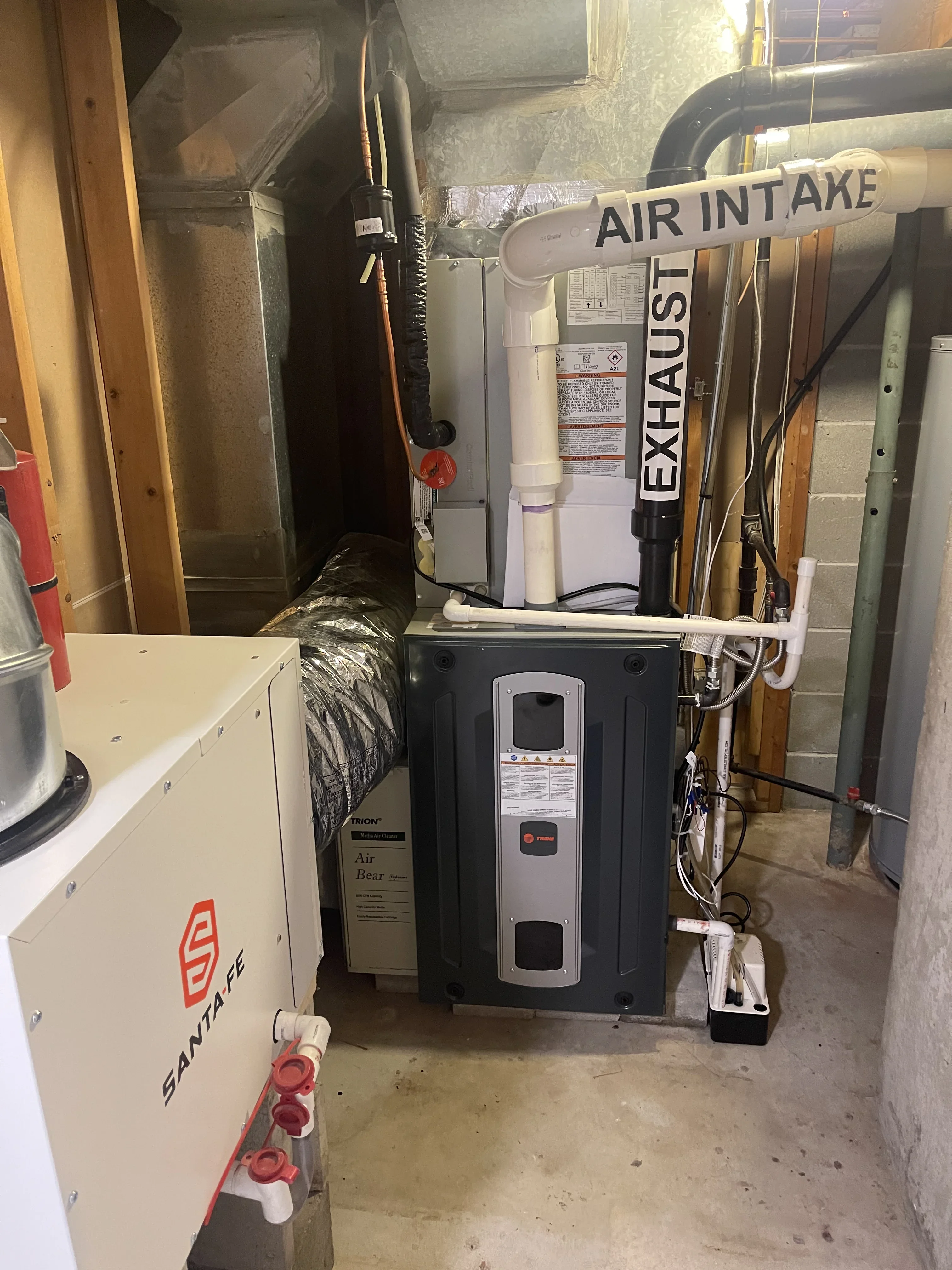 Heat pump unit with air intake and exhaust ducts, electrical wiring, and dehumidifier system installed in basement