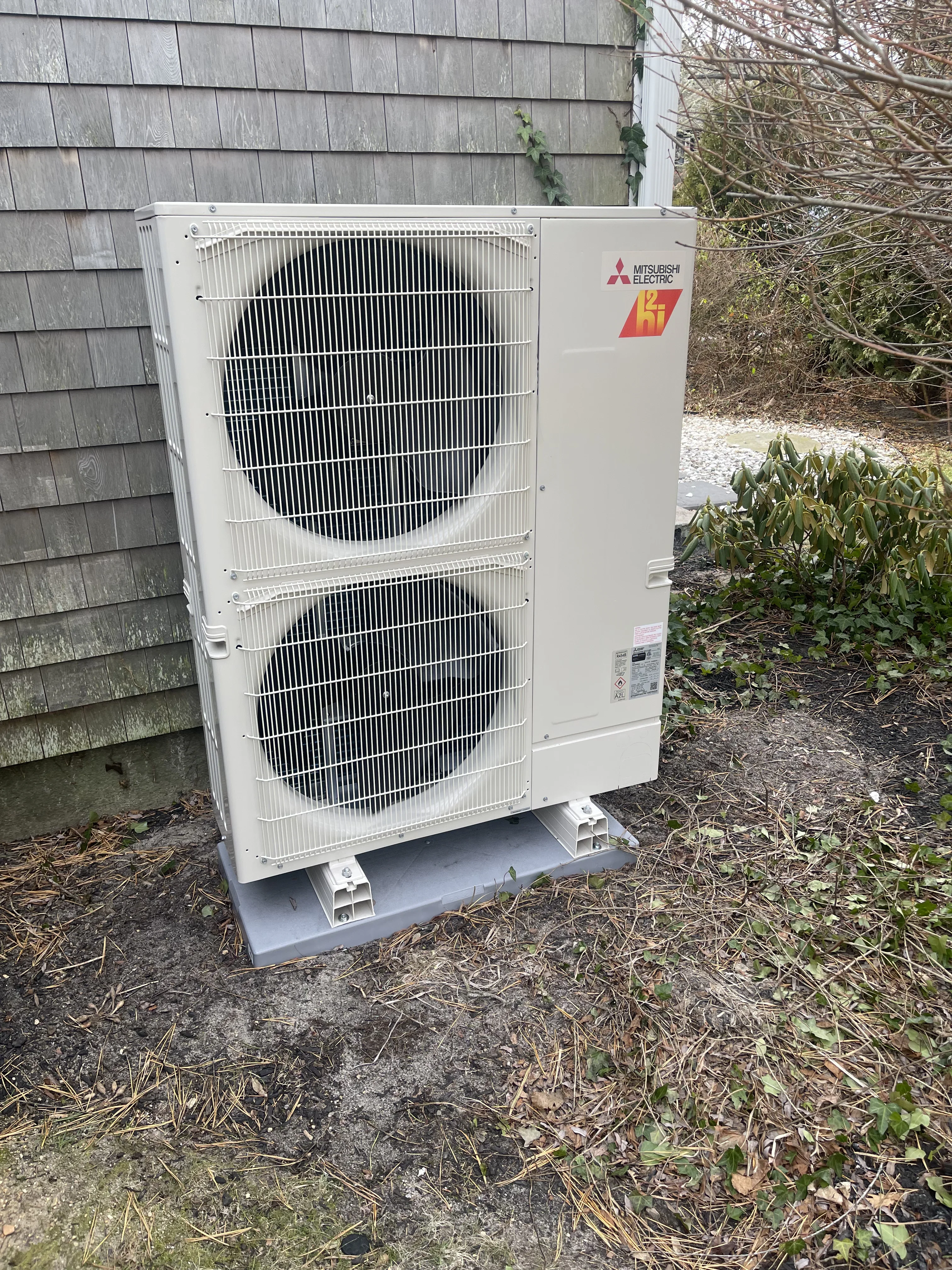 White Mitsubishi Electric heat pump unit with dual condenser coils installed on concrete pad