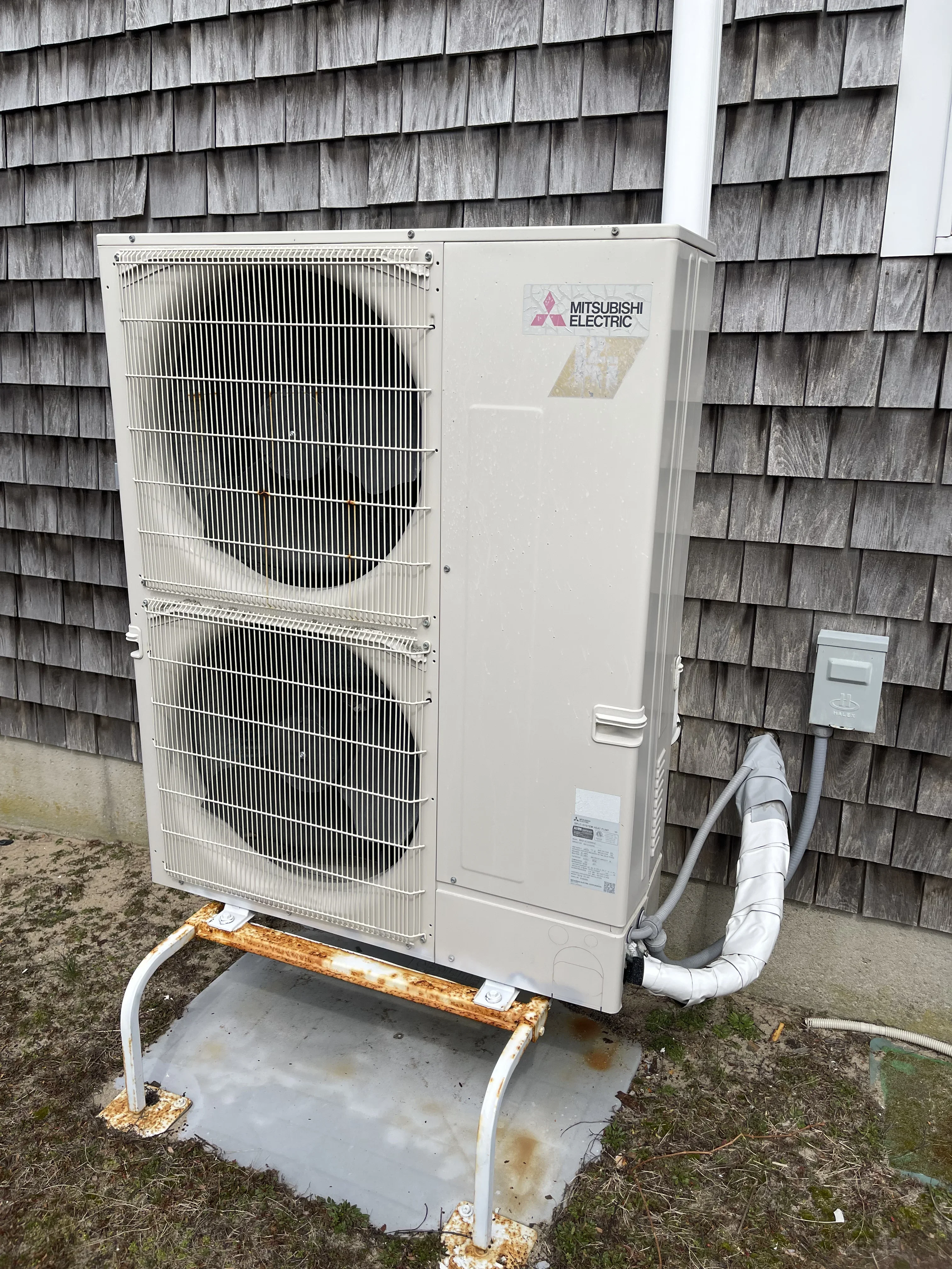 Mitsubishi Electric heat pump condenser unit installed on concrete pad against cedar shake siding